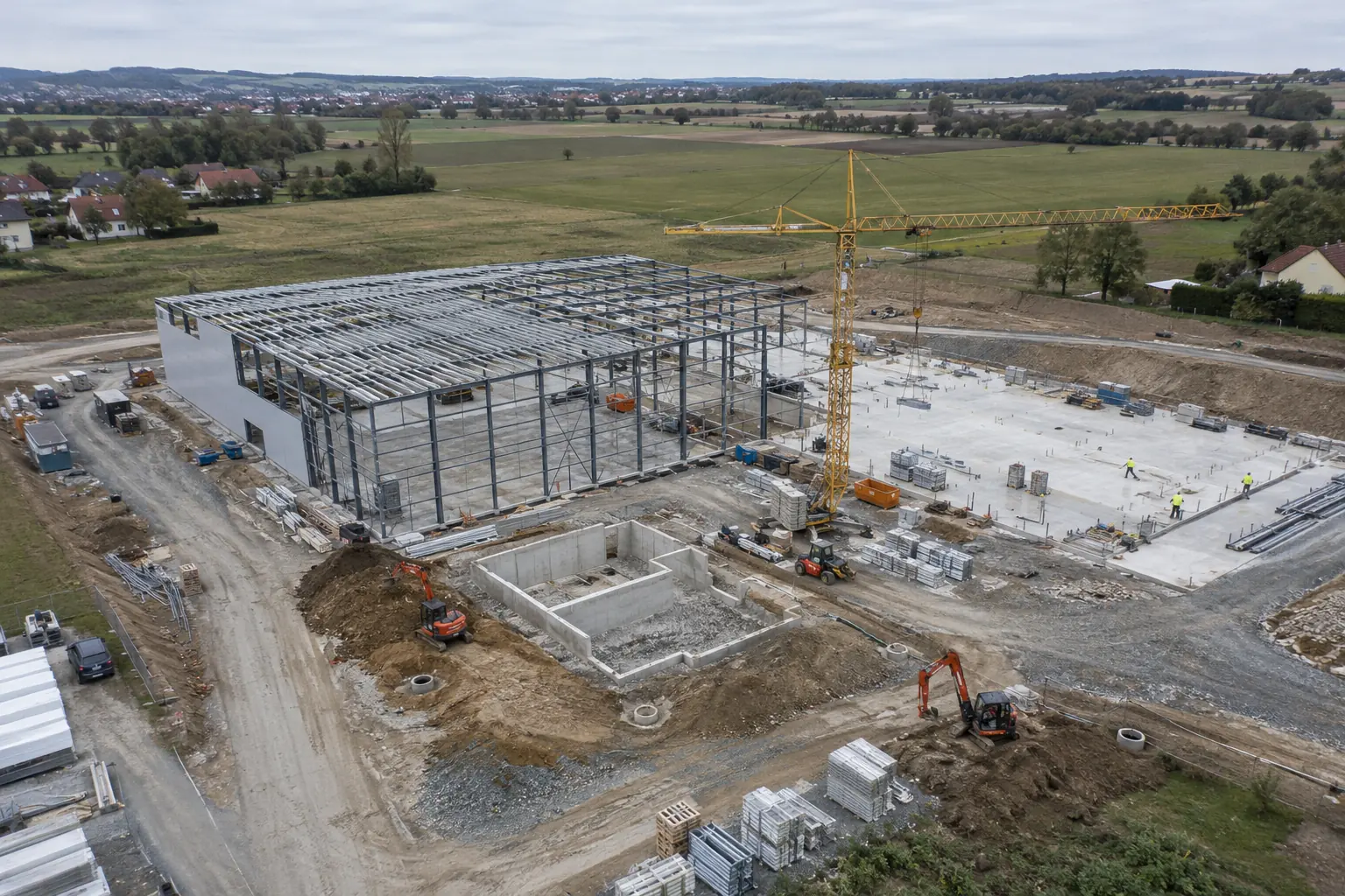Luftbild einer Gewerbebaustelle mit Stahlhalle, Turmdrehkran und Bodenplatten