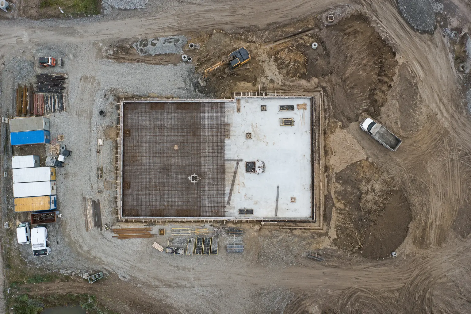 Senkrechte Luftaufnahme einer Baustelle mit Bodenplatte, Baugrube und Baustelleneinrichtung